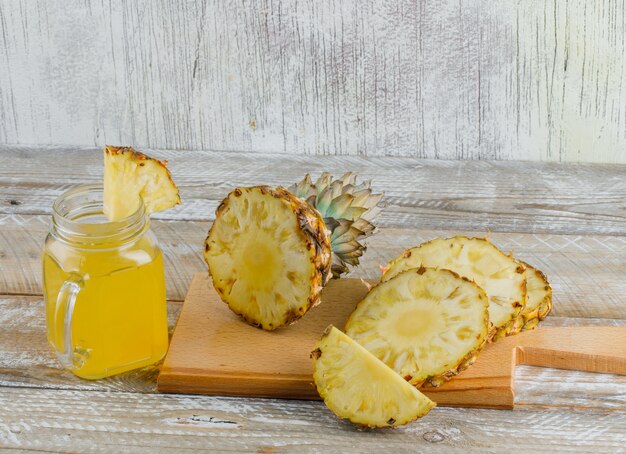 Piña con jugo y tabla de cortar sobre madera y superficie sucia