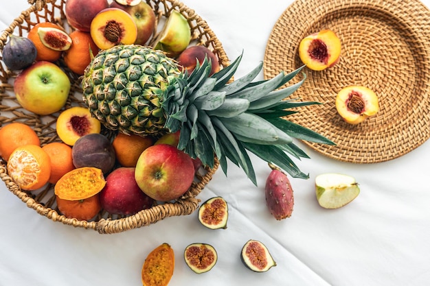Piña y otras frutas exóticas en una cesta de mimbre sobre un fondo blanco.