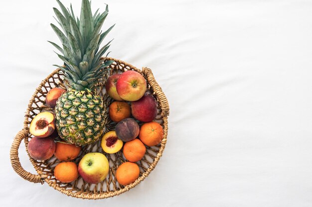 Piña y otras frutas exóticas en una cesta en una vista superior de fondo blanco