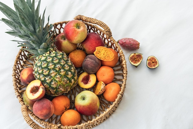 Piña y otras frutas exóticas en una cesta en una vista superior de fondo blanco