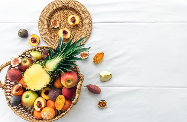 Piña y otras frutas exóticas en una cesta en una vista superior de fondo blanco