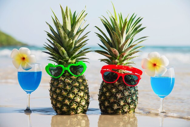 Piñas frescas de los pares con los vidrios de sol y los vidrios de cóctel en la playa limpia de la arena con la onda del mar - fruta fresca y bebida con concepto de las vacaciones del sol de la arena de mar