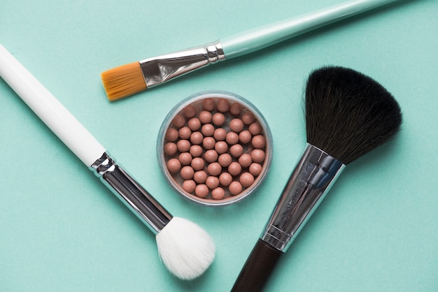 Pincel de maquillaje con perlas bronceadas sobre fondo verde