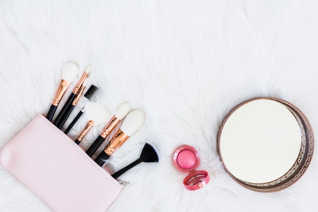 Pinceles de maquillaje en bolsa con polvo compacto rosa y espejo redondo sobre fondo de piel