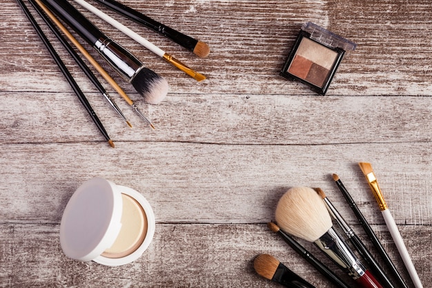 Pinceles para maquillaje y productos cosméticos sobre fondo de madera. En la vista de imagen superior