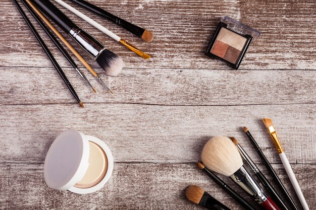 Pinceles para maquillaje y productos cosméticos sobre fondo de madera. En la vista de imagen superior