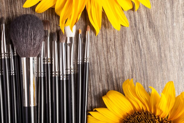 Pinceles de maquillaje profesional junto a hermosas flores silvestres sobre fondo de madera