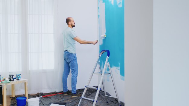 Pintar la pared del apartamento con pintura blanca con un cepillo de rodillo. Manitas renovando. Redecoración de apartamentos y construcción de viviendas mientras se renueva y mejora. Reparación y decoración.