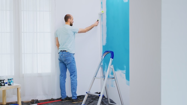Pintar la pared azul con pintura blanca con un cepillo de rodillo durante la renovación de la casa. Manitas renovando. Redecoración de apartamentos y construcción de viviendas mientras se renueva y mejora. Reparación y decoración.