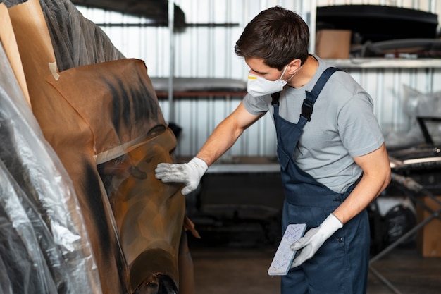 Foto gratuita pintor masculino en overoles haciendo su trabajo en la tienda de autos