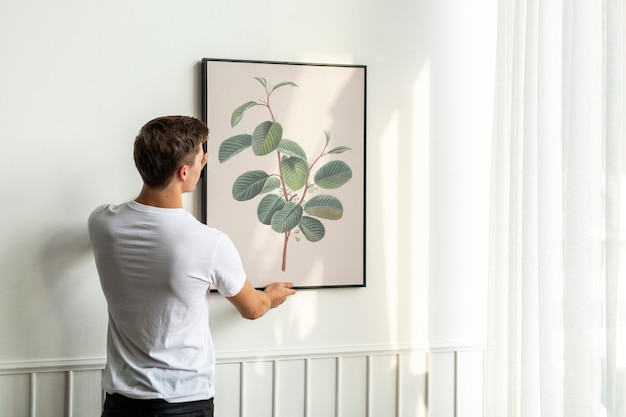 Foto gratuita pintura de hoja vintage colgada por un joven en una pared mínima blanca