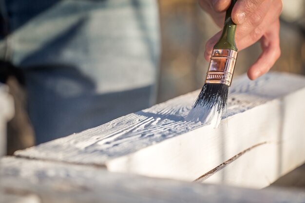 Pinturas de manos masculinas con pintura blanca sobre madera, concepto de pintura, primer plano, lugar para el texto