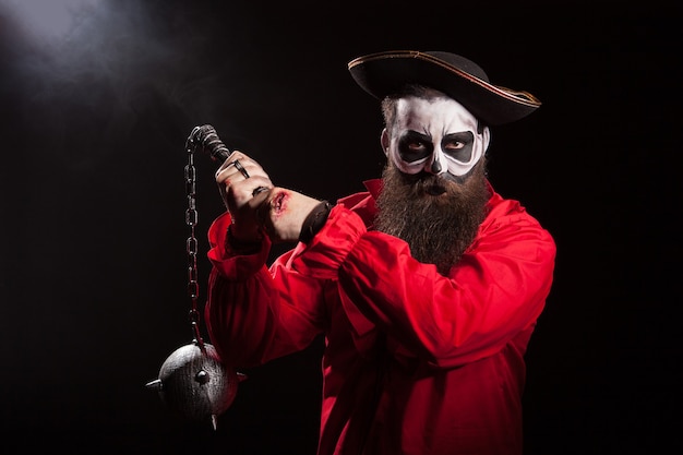 Pirata hombre espeluznante con barba larga sosteniendo una maza sobre fondo negro. Traje de Halloween.
