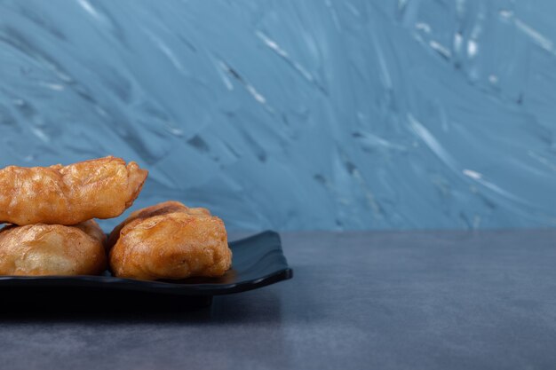 Pirozhki de pastelería rusa recién horneada en placa de madera sobre mesa de mármol.