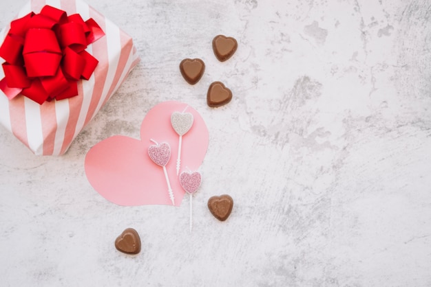 Piruletas cerca de dulces de chocolate, corazón de papel y caja de regalo