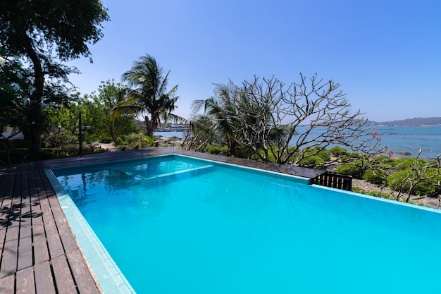 Piscina de agua azul y jardín tropical con fondo de vista al mar.