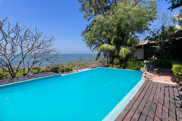 Piscina de agua azul y jardín tropical con fondo de vista al mar.