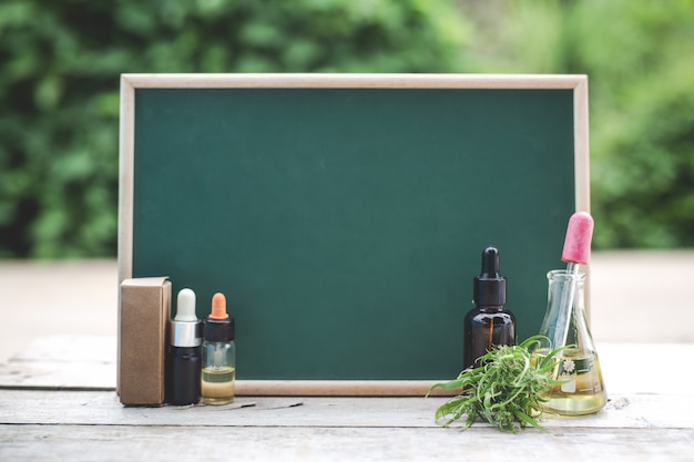 Foto gratuita en el piso de madera hay aceite de cáñamo, hoja de cáñamo y el tablero verde está en blanco para poner texto.