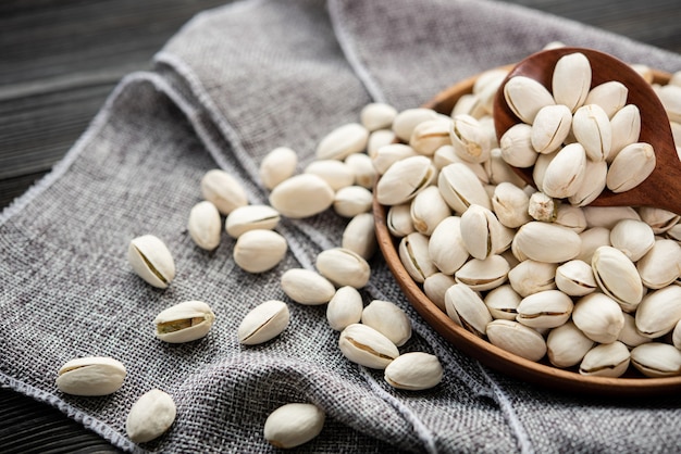 Pistachos en una cuchara de madera. Cuenco de madera con pistachos de nuez. sobre un fondo de madera, cerca de una bolsa de arpillera. Comida sana y merienda, comida vegetariana orgánica.