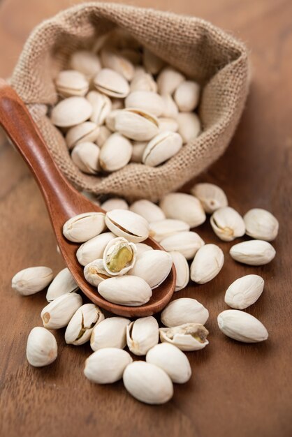 Pistachos en una cuchara de madera. Saco con pistachos sobre una mesa de madera.