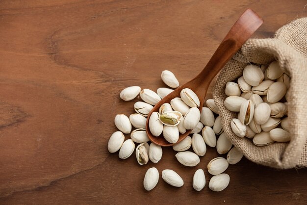 Pistachos en una cuchara de madera. Saco con pistachos sobre una mesa de madera.