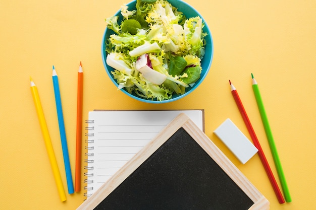 Foto gratuita pizarra y artículos de papelería cerca de plato de ensalada