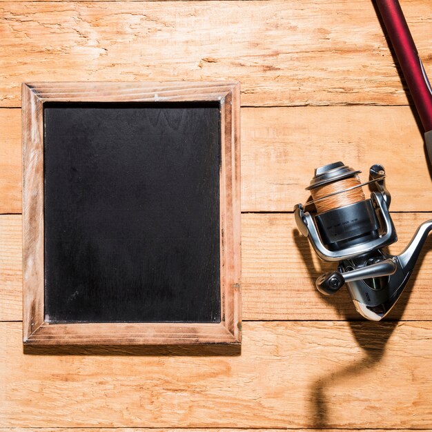 Pizarra en blanco con carrete de pesca en mesa de madera