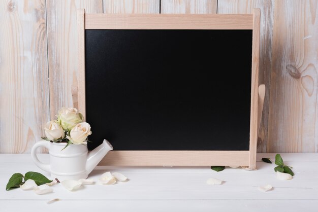 Pizarra en blanco con hermosas rosas en mesa de madera