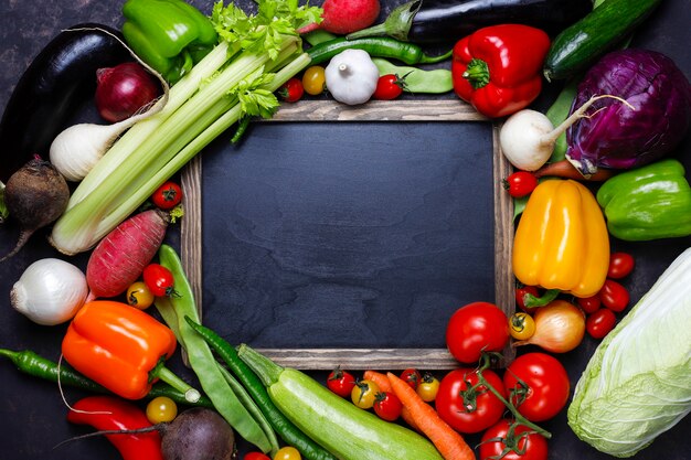 Pizarra con diferentes vegetales saludables coloridos sobre fondo oscuro