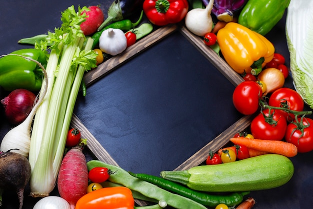 Pizarra con diferentes vegetales saludables coloridos sobre fondo oscuro