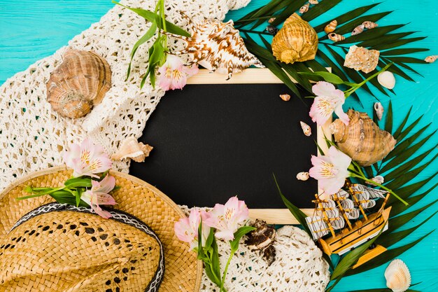 Pizarra entre las hojas de la planta con flores cerca de conchas y sombrero