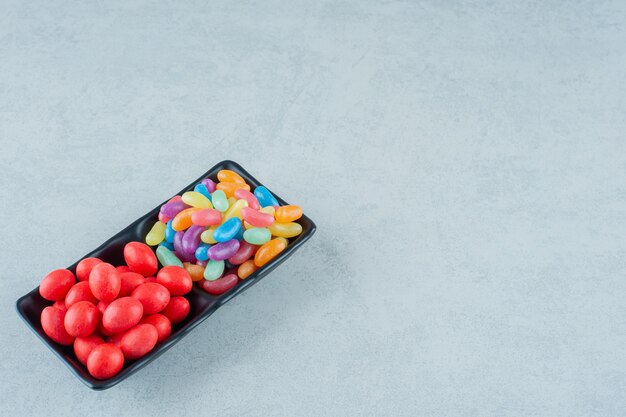 Una pizarra llena de caramelos de frijoles coloridos sobre una superficie blanca