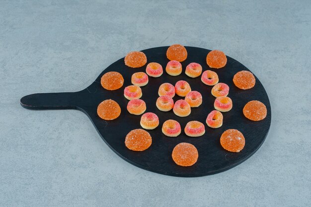 Una pizarra llena de caramelos de gelatina de naranja redondos en forma de anillos y caramelos de gelatina de naranja con azúcar