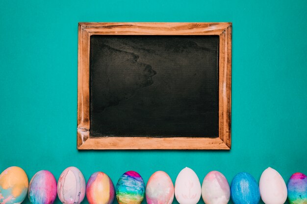 Pizarra de madera sobre la fila de huevos de Pascua pintados sobre fondo verde