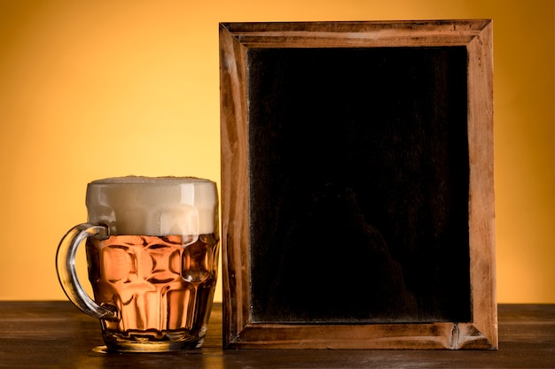 Pizarra vacía con vaso de cerveza en la mesa de madera