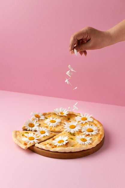 Pizza de alto ángulo con flores sobre fondo rosa