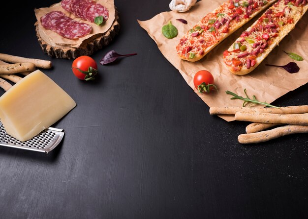 Pizza de baguette con ingredientes de comida italiana sobre superficie de piedra negra