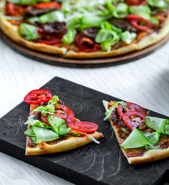 Pizza de carne con rodajas de tomate y pepino fresco