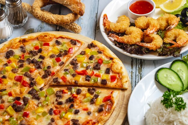 Pizza de carne de vista lateral con pimientos rojos amarillos y verdes queso de carne y camarones tempura sobre la mesa