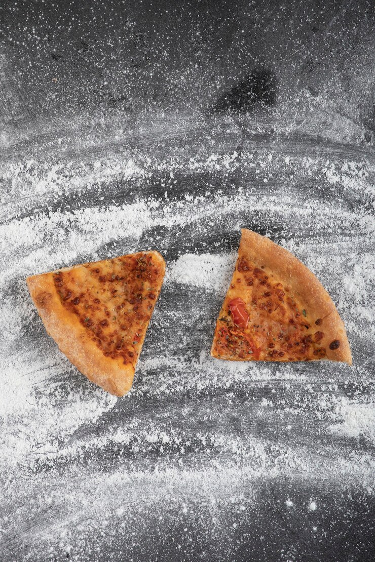 Foto gratuito pizza casera en rodajas sobre superficie negra con harina de trigo derramada