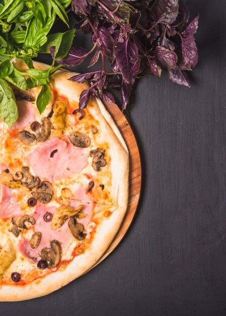 Pizza de champiñones y carne sobre tabla de madera con verduras de hoja