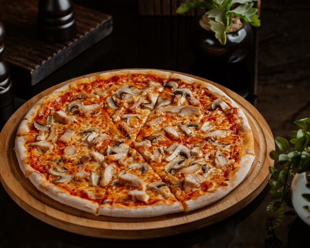 Pizza de champiñones con salsa de tomate y servida en una tabla redonda de bambú