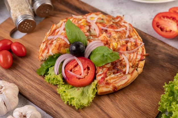 La pizza está en una bandeja de madera cubierta con cebollas rojas, uvas negras, tomates y lechuga.