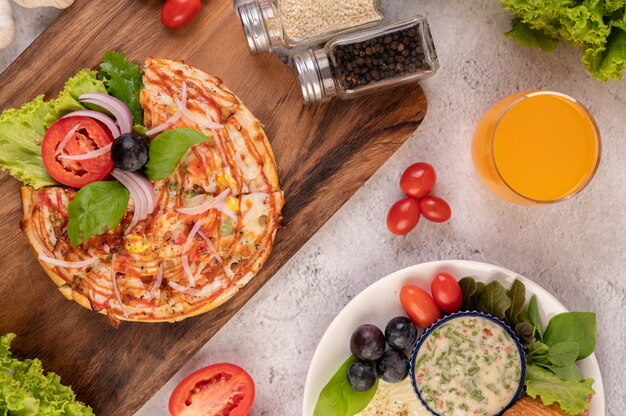 La pizza está en una bandeja de madera cubierta con cebollas rojas, uvas negras, tomates y lechuga.