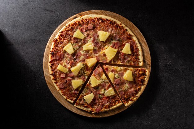 Pizza hawaiana con piña y queso sobre fondo de pizarra negra