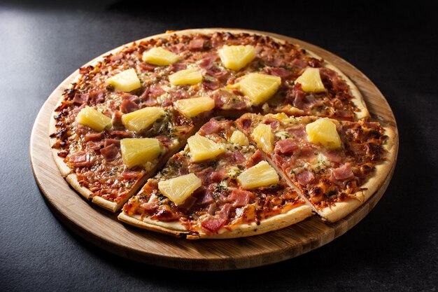 Pizza hawaiana con piña y queso sobre fondo de pizarra negra