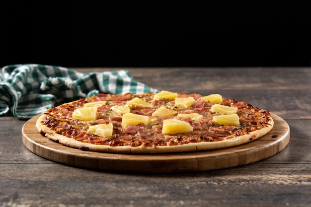 Pizza hawaiana con piña y queso sobre mesa de madera