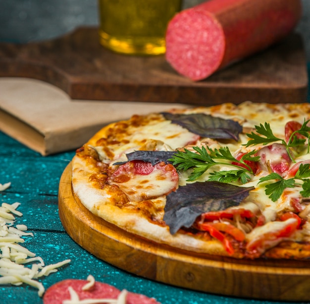 Pizza de ingredientes mixtos con hojas basílicas rojas y tomate.