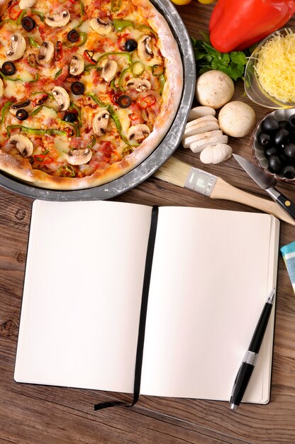 Pizza con el libro de cocina e ingredientes en blanco