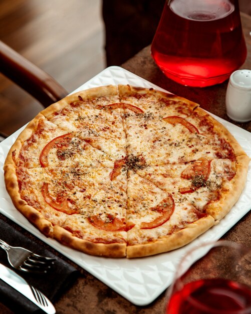 Pizza de margarita adornada con rodaja de tomate y hojas de menta secas